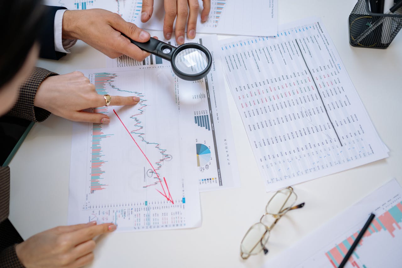 ours-journey Business professionals examining financial documents with magnifying glass for detailed analysis.